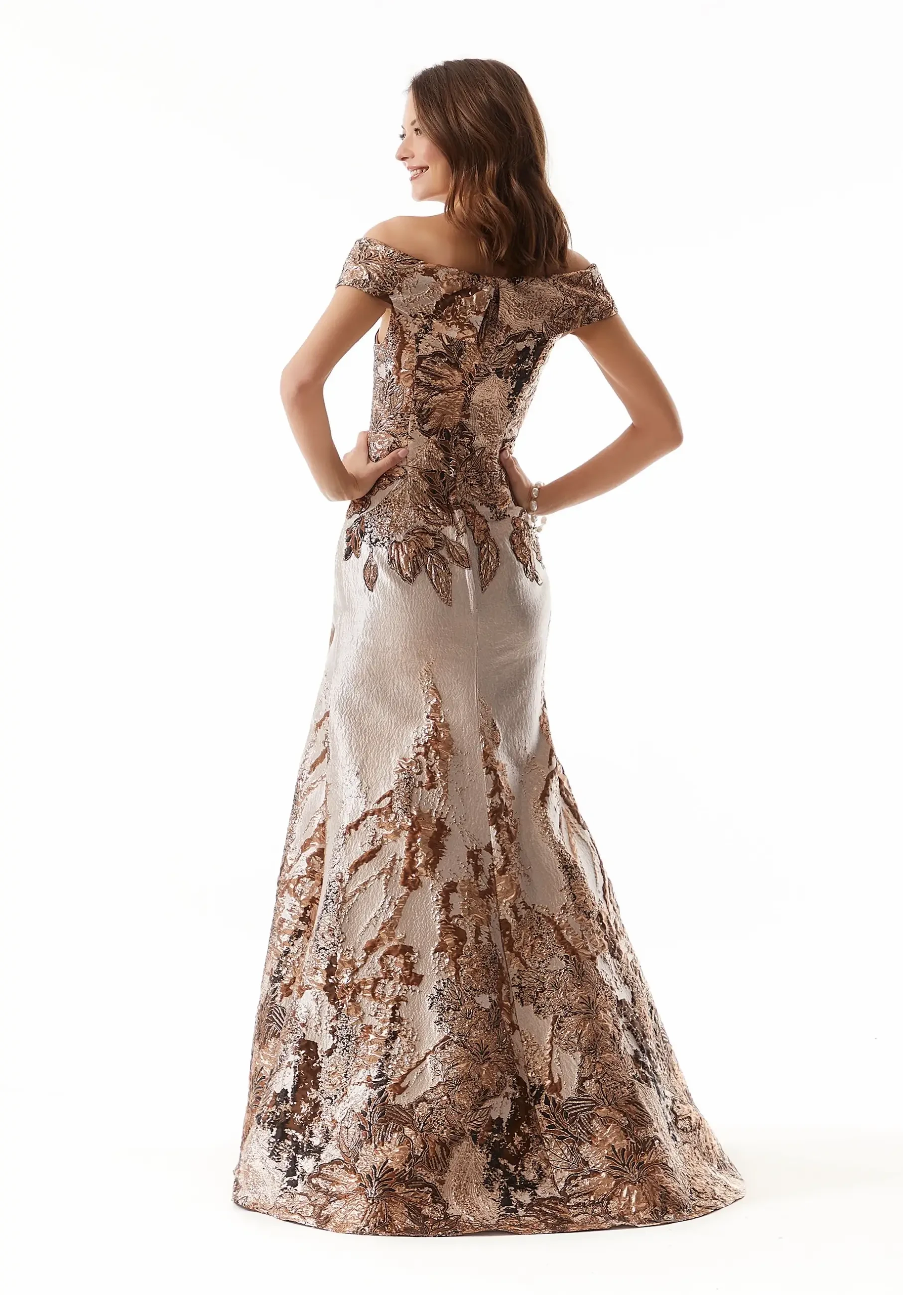 Model is wearing a full length evening gown made of metallic jacquard fabric with delicate cuffed detail