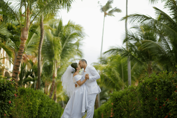 Bride and groom embracing in a tropical garden resort surrounded by palm trees during a destination wedding.