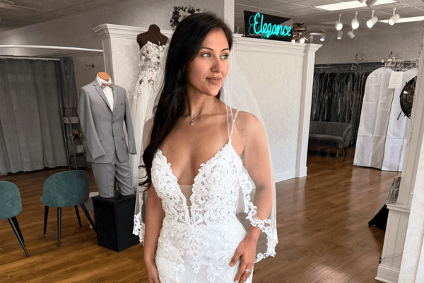 Bride wearing a lace wedding dress with a deep V neckline and sheer sleeves inside a bridal boutique