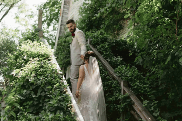 Bride and groom walking up the stairs at Blue Dress Barn, groom holding the bride&rsquo;s hand, plants on either side