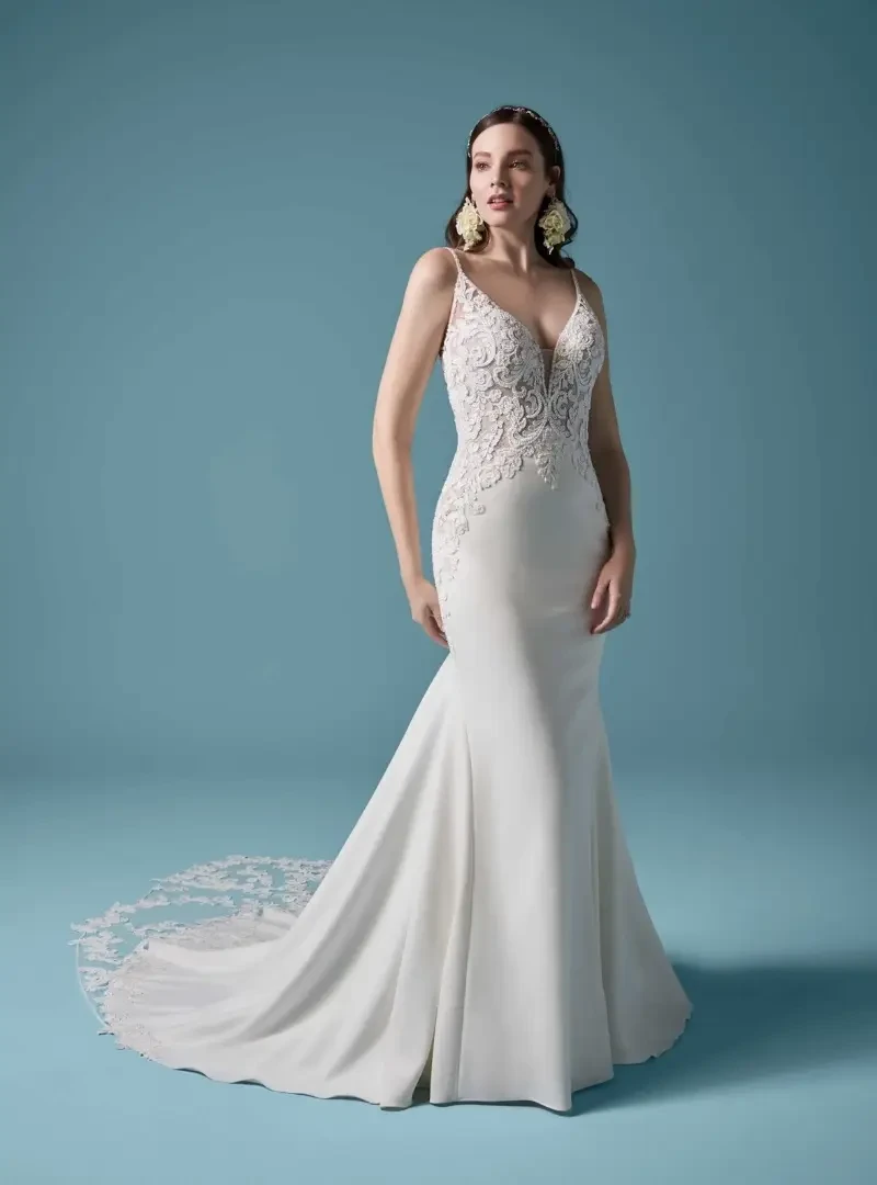 Model wearing a fitted wedding dress with a lace V-neck bodice, spaghetti straps, and a flared skirt with lace train.