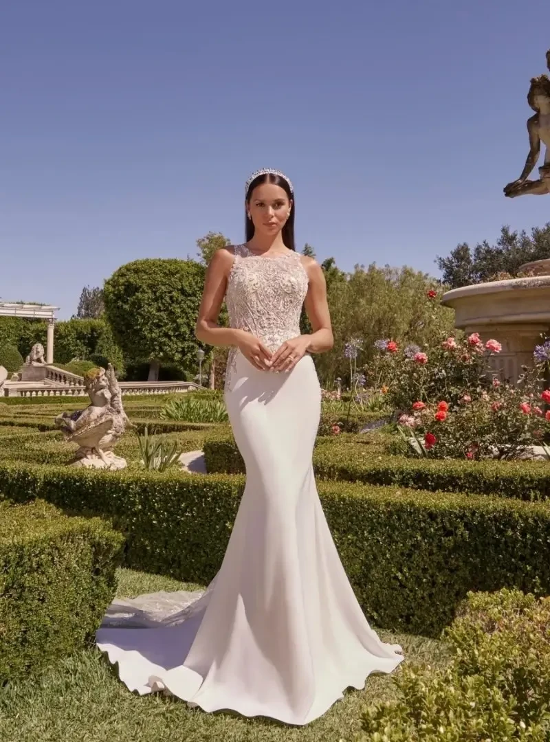 Model wearing a fitted wedding dress with an intricate beaded lace bodice, high neckline, and sleek flared skirt.