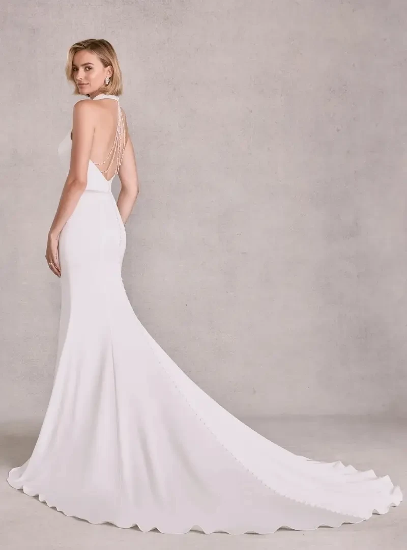 Back view of a fitted wedding dress with an open back, draped beading, covered buttons, and a long train.