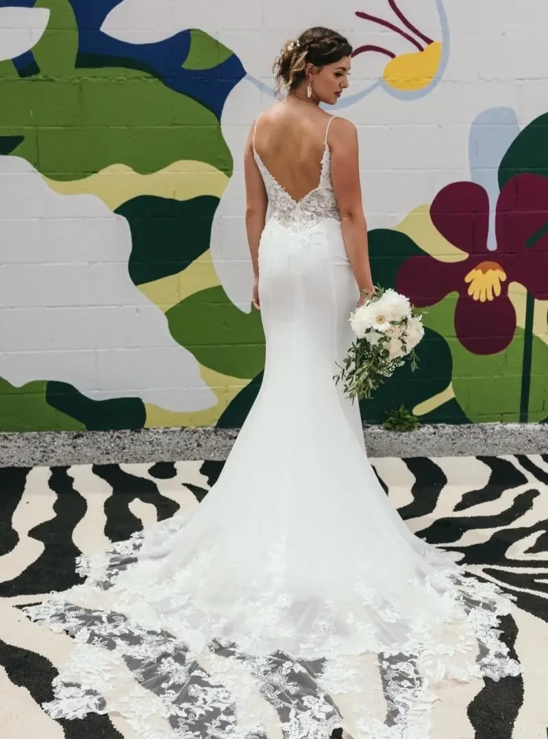 Back view of a fitted wedding dress with a low open back, lace detailing, spaghetti straps, and a long floral lace train.