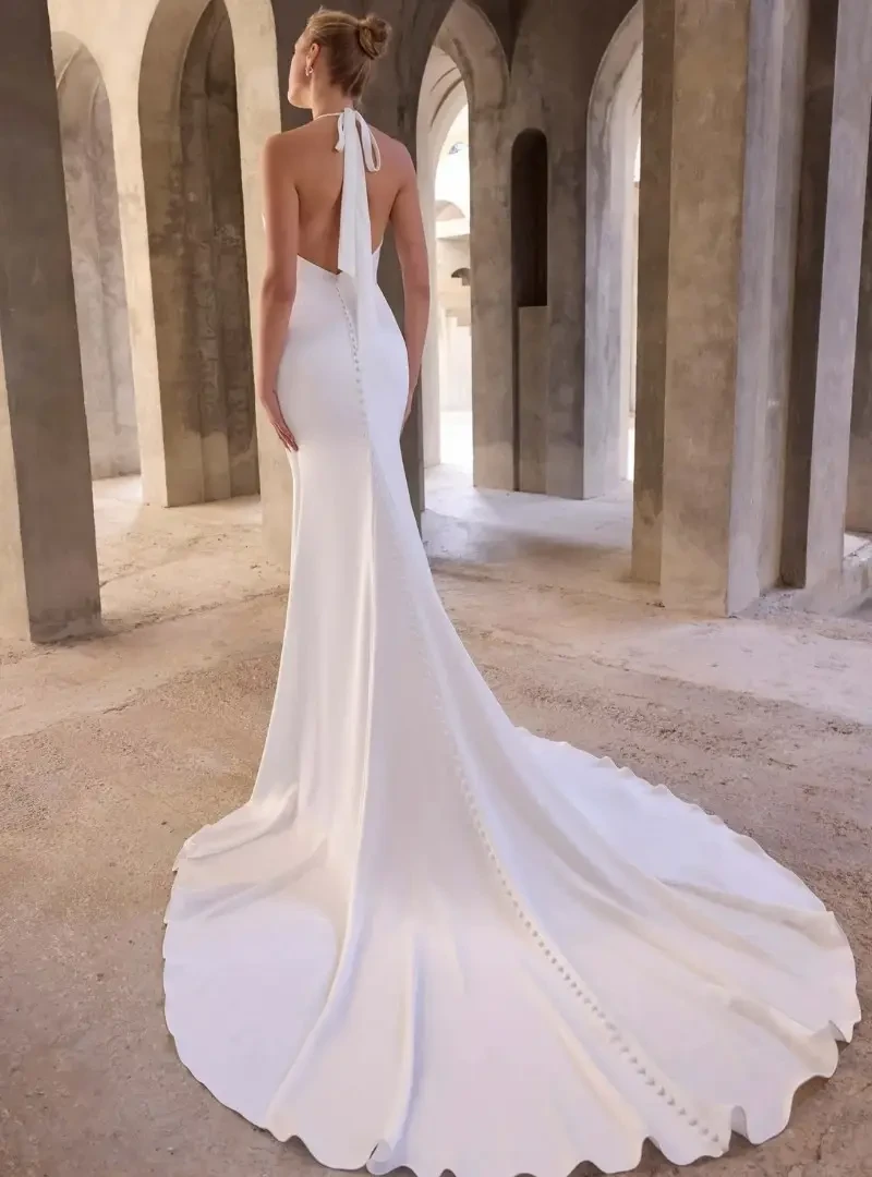 Back view of a fitted halter wedding dress with an open back, covered buttons, and a long flowing train.