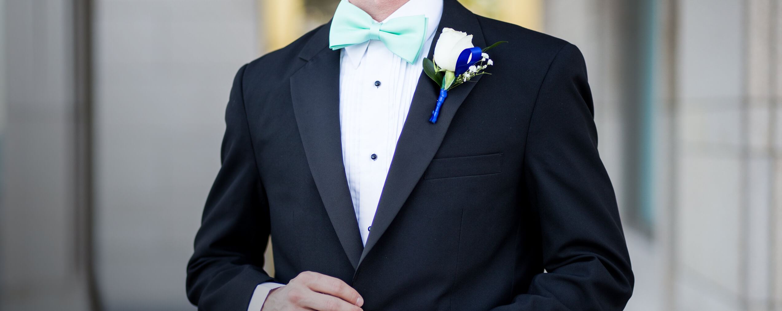 Male model wearing black tuxedo and mint blue bow tie on desktop